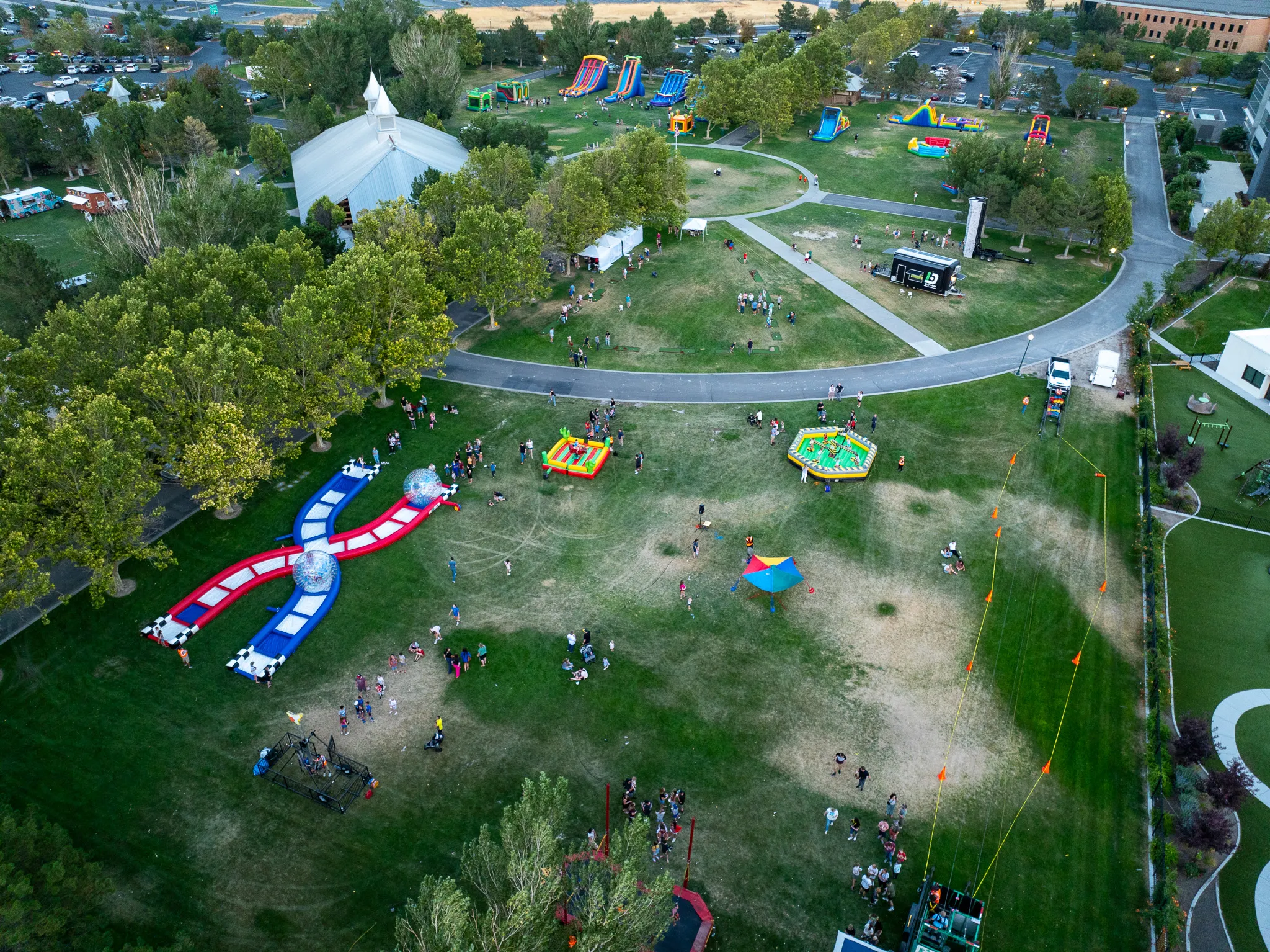 Aerial drone shot of an outdoor community festival with bounce houses and crowds in an American Fork park, Utah