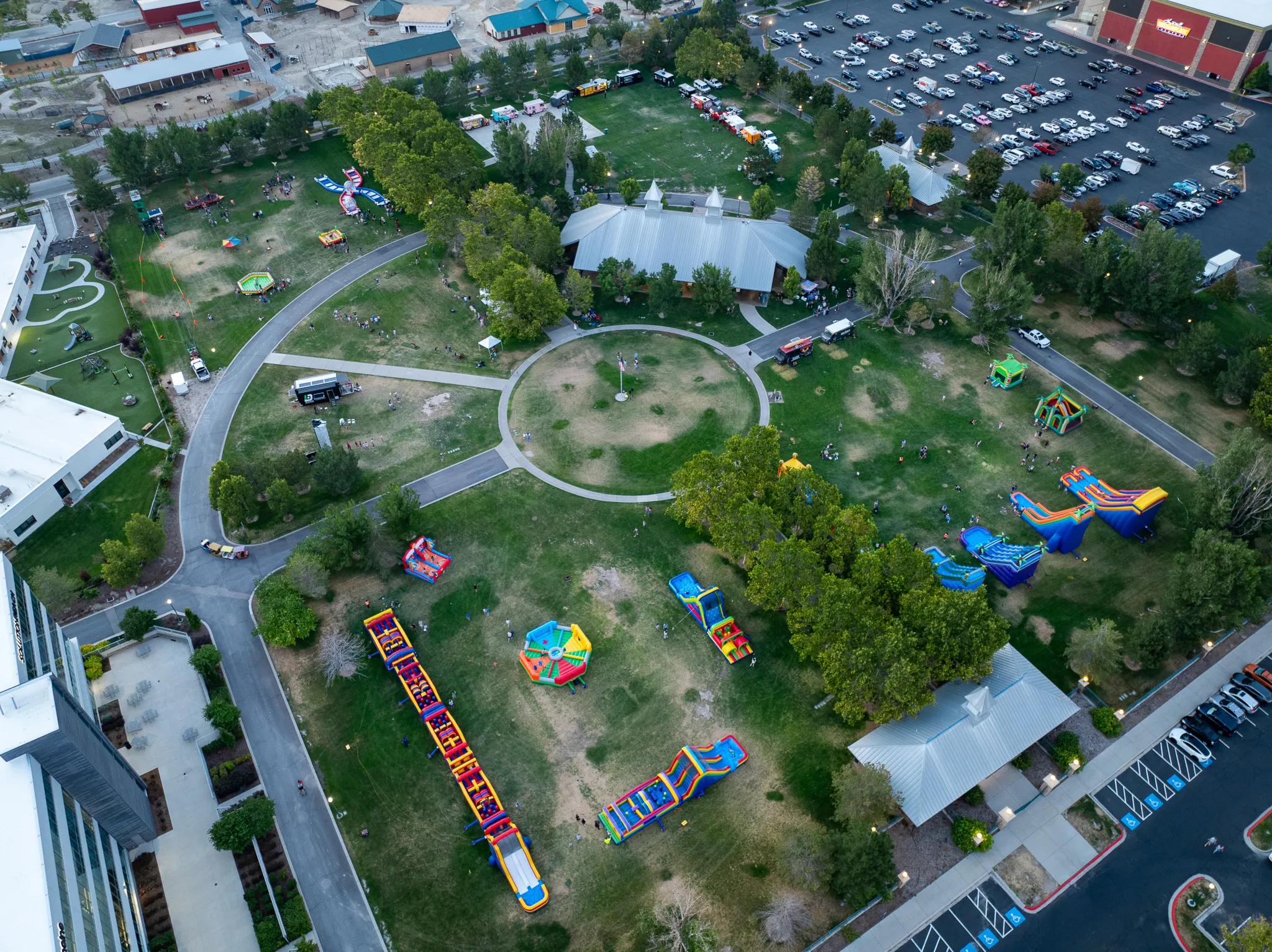 Wide drone view of a Utah community festival venue with inflatable attractions, food trucks, and parking, Utah County